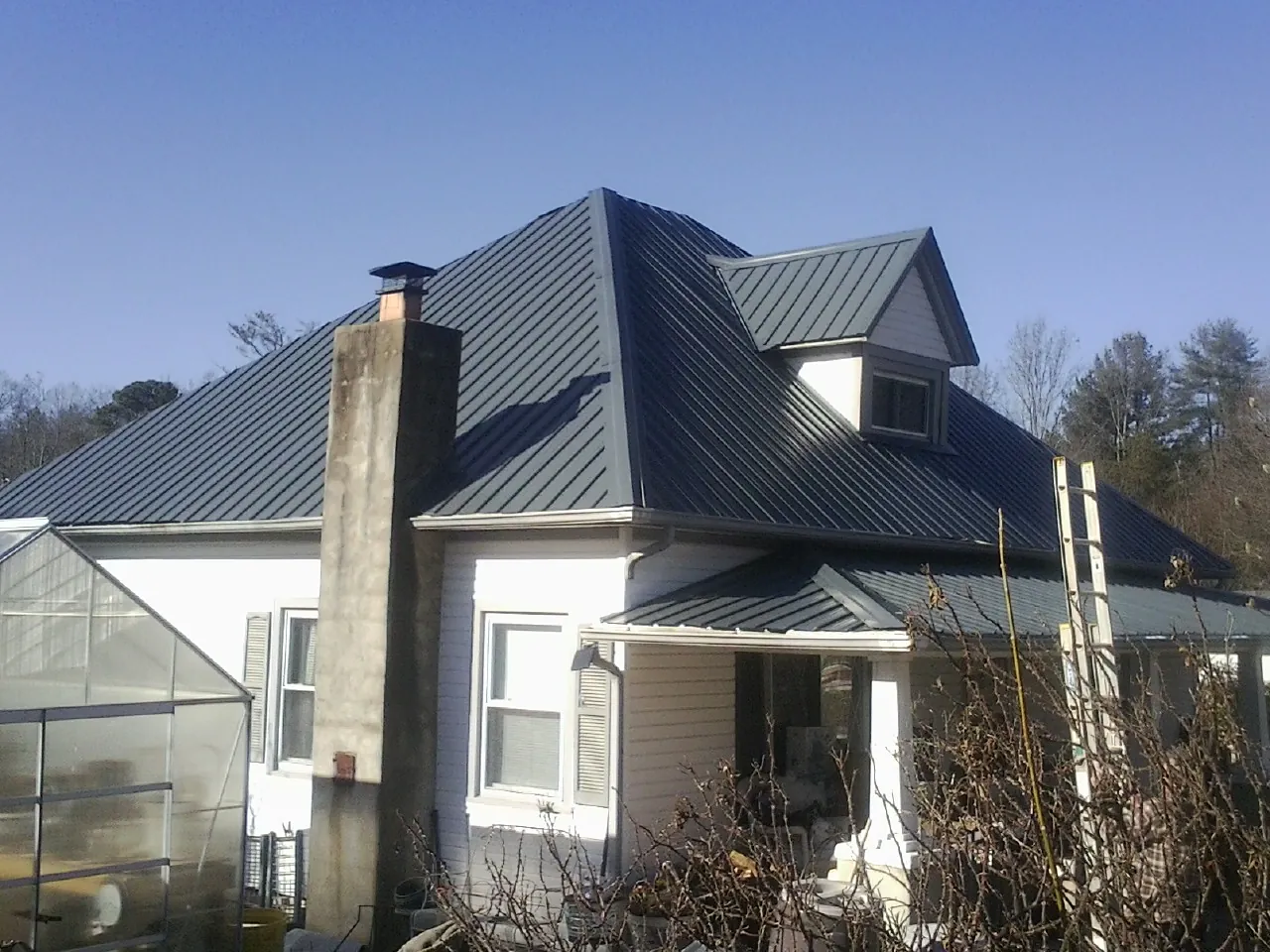 Dark blue standing seam metal roof on a white farmhouse with dormer — Slate & Tile Roof Repair by Roofing Brothers in New York Mills
