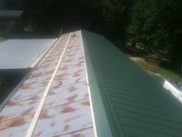 Old rusted panels beside newly installed green metal roofing — Wind Damage Roof Repair by Roofing Brothers in New York Mills
