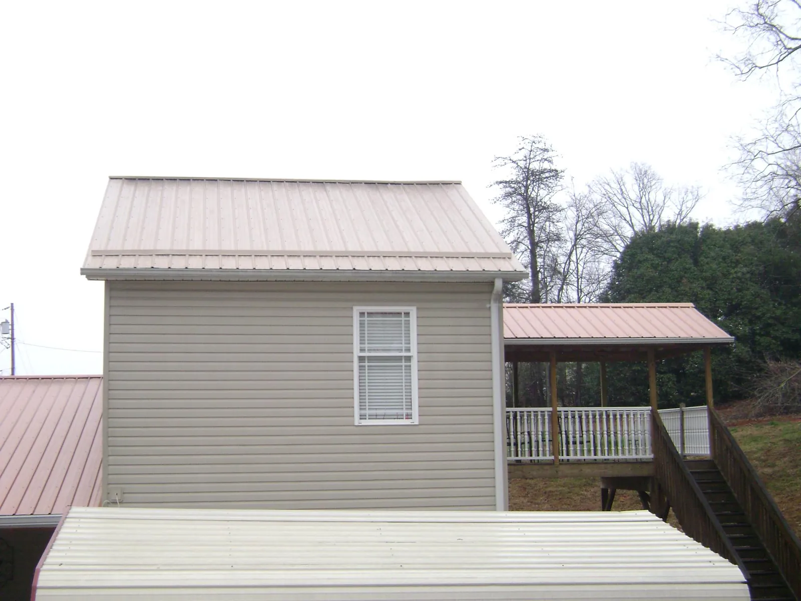 Tan metal roofs on a two story addition and attached porch, from a Roof Replacement job in New York Mills